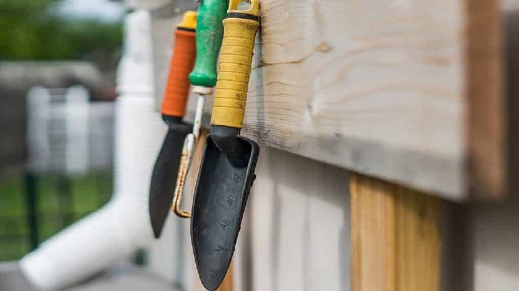 A garden trowel and other tools handing on a wooden board.